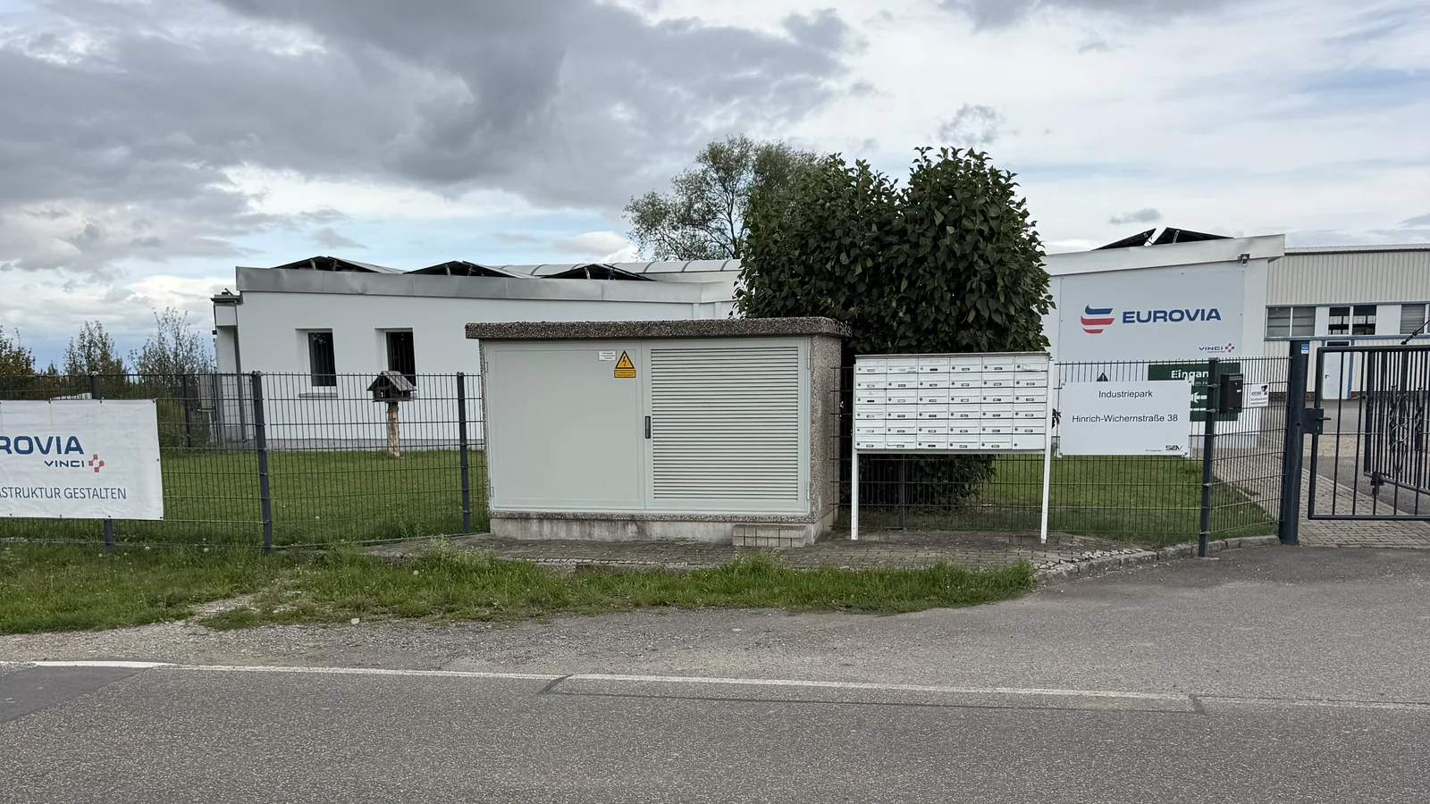 Zufahrt zum Gewerbepark mit Tor, Firmenschildern und Gebäuden