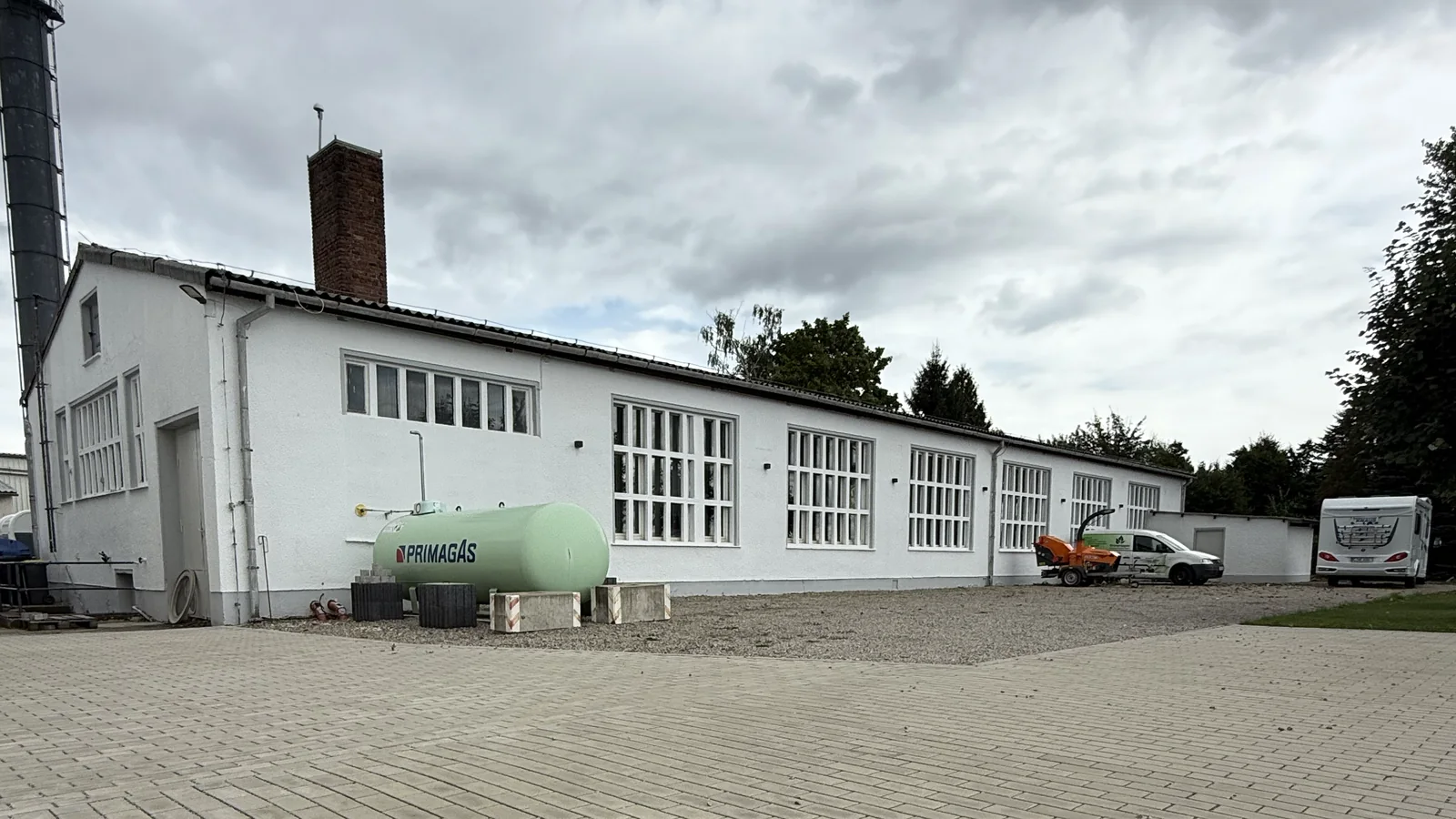 Lange Hallenfassade mit hohen Fenstern und gepflastertem Vorplatz